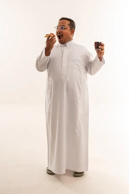 رجل سعودي بالثوب يتناول البيتزا والمشروب الغازي