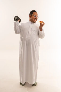 رجل عربي بوزن زائد يحمل دمبل وقطعة بيتزا