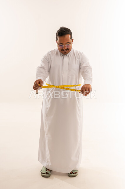 رجل سعودي سمين يقيس خصره في استوديو خلفية بيضاء