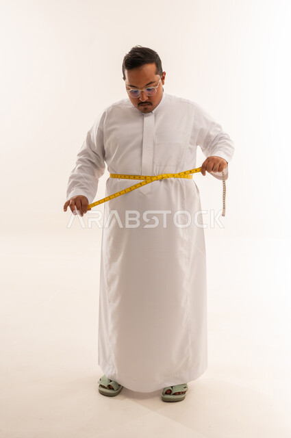 رجل عربي يعاني من السمنة يقيس خصره بالثوب الأبيض
