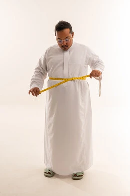 رجل عربي يعاني من السمنة يقيس خصره بالثوب الأبيض