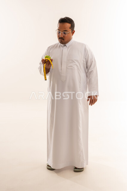 رجل سعودي مع تفاحة وشريط قياس لمفهوم الدايت