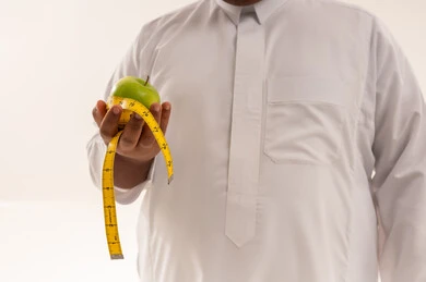 رجل عربي يحمل تفاحة وشريط قياس للوزن