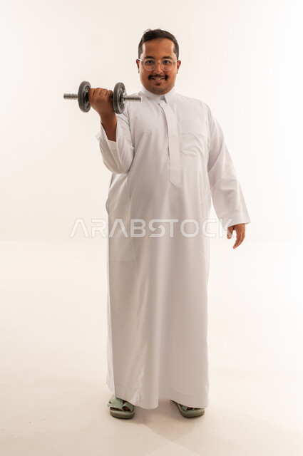 رجل سعودي يرتدي الثوب يرفع الدبل في استوديو أبيض