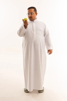 رجل سعودي بالثوب يحمل تفاحة خضراء في استوديو