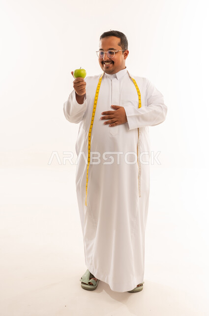 رجل سعودي سمين مع تفاحة خضراء وشريط قياس