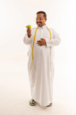 رجل سعودي سمين مع تفاحة خضراء وشريط قياس