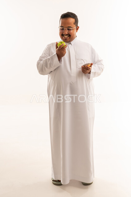 رجل سعودي بالثوب يحمل تفاحة ودونات في الاستوديو