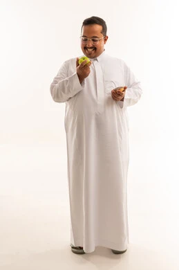 رجل سعودي بالثوب يحمل تفاحة ودونات في الاستوديو