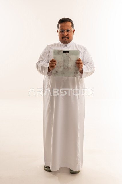 رجل سعودي سمين يحمل ميزان وزن بخلفية بيضاء
