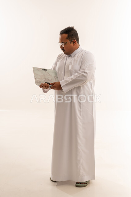 رجل سعودي سمين يمسك ميزان في الاستوديو