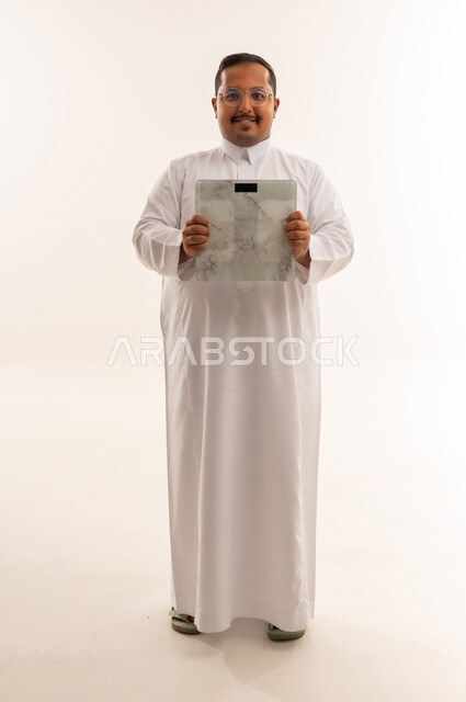 رجل سعودي يحمل ميزان وزن على خلفية بيضاء