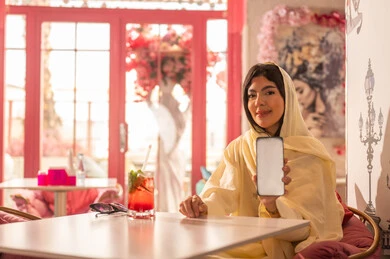 Saudi Woman Holding Blank Smartphone in Pink Cafe