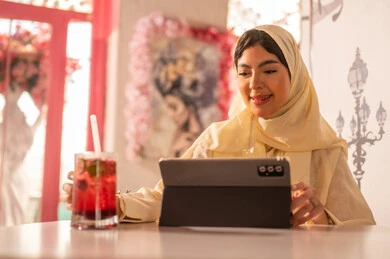 Saudi Woman Using Tablet in Cafe with Cold Drink