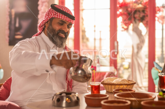 رجل سعودي بالزي التقليدي يسكب الشاي في مقهى