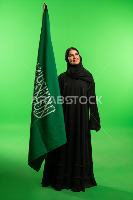 امرأة سعودية بالعباءة مع العلم أمام خلفية خضراء
