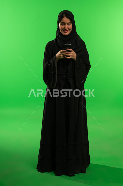 امرأة سعودية بالعباءة السوداء تستخدم الهاتف أمام كروما خضراء