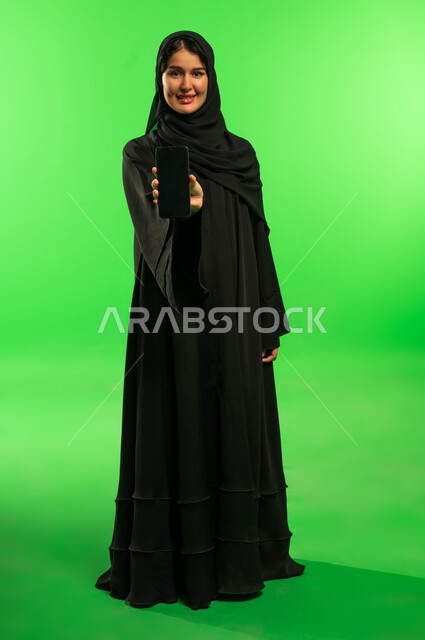 امرأة سعودية تحمل هاتفاً ذكياً بخلفية كروما خضراء