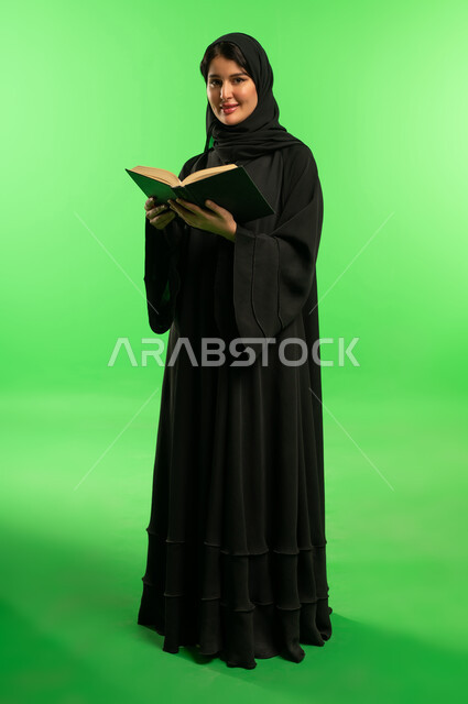 امرأة سعودية بالعباءة مع كتاب أمام خلفية خضراء