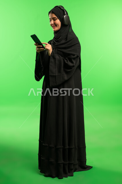 امرأة سعودية تستخدم الهاتف مع سماعات على خلفية خضراء