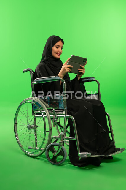 امرأة سعودية على كرسي متحرك مع جهاز لوحي خلفية خضراء