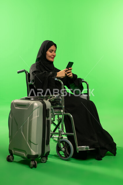 امرأة سعودية على كرسي متحرك مع حقيبة سفر كروما خضراء