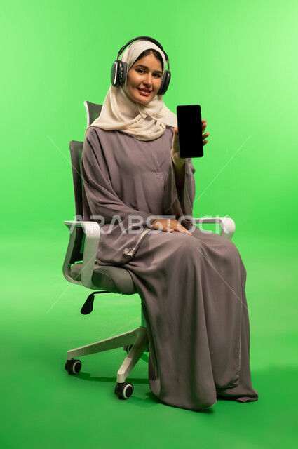 امرأة سعودية مع هاتف وسماعات على خلفية خضراء