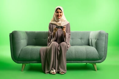 امرأة سعودية مع جهاز تحكم ألعاب بخلفية خضراء