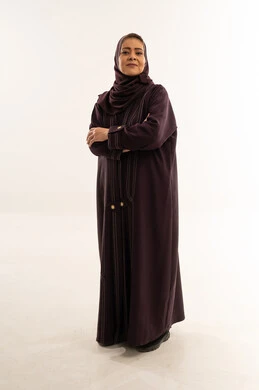 امرأة سعودية بعباءة أرجوانية أمام خلفية بيضاء