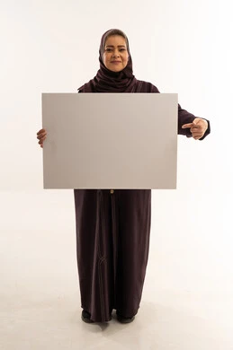 امرأة سعودية بعباءة أرجوانية تمسك لوحة بيضاء فارغة