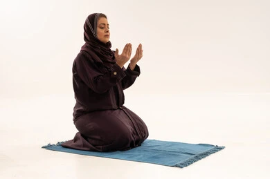 امرأة عربية بالعباءة تدعو على سجادة صلاة بخلفية بيضاء