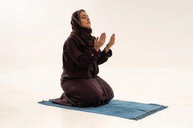 امرأة مسلمة بالعباية تدعو على سجادة الصلاة