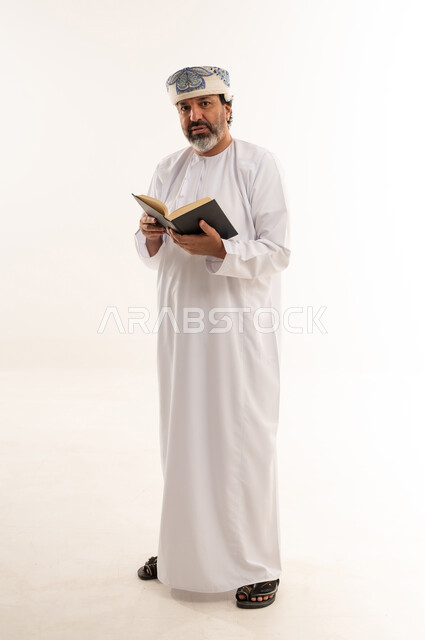 رجل عماني بالزي التقليدي يقرأ كتاباً في الاستوديو
