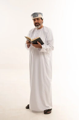 رجل عماني بالزي التقليدي يقرأ كتاباً في الاستوديو