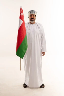 رجل عماني بالزي التقليدي يحمل علم سلطنة عمان