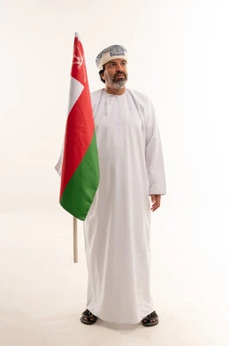 رجل عماني بالزي التقليدي يقف مع علم السلطنة