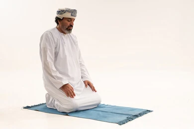رجل عماني يصلي على سجادة زرقاء خلفية بيضاء