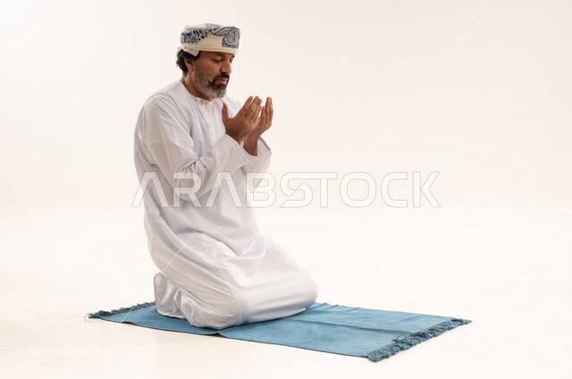 رجل عماني يصلي على سجادة بخلفية بيضاء