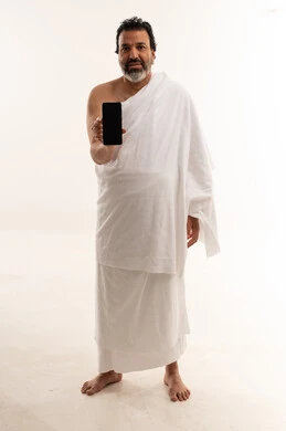 رجل عربي بملابس الإحرام يحمل هاتفاً ذكياً