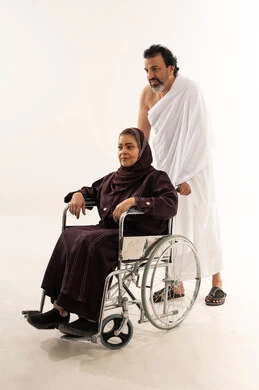 رجل سعودي بملابس الإحرام يدفع امرأة على كرسي متحرك