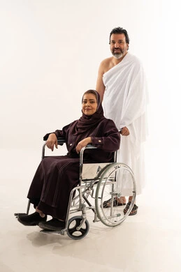 رجل سعودي وامرأة مسنة على كرسي متحرك بملابس الإحرام