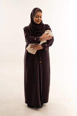 أم سعودية بعباءة بنفسجية تحمل طفلاً حديث الولادة