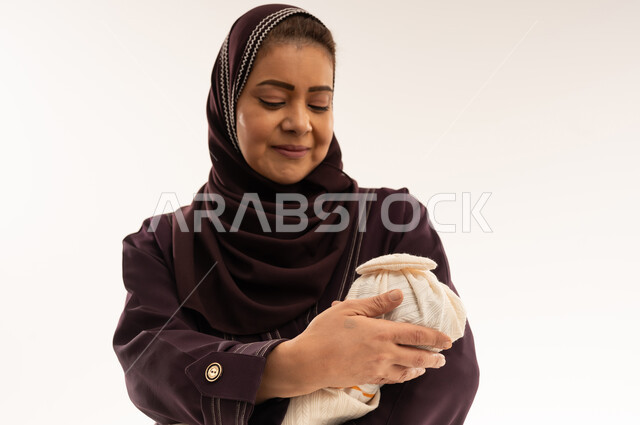امرأة عربية بعباءة أرجوانية تحمل طفلاً حديث الولادة