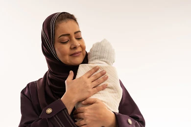 أم سعودية تحتضن مولودها الجديد على خلفية بيضاء