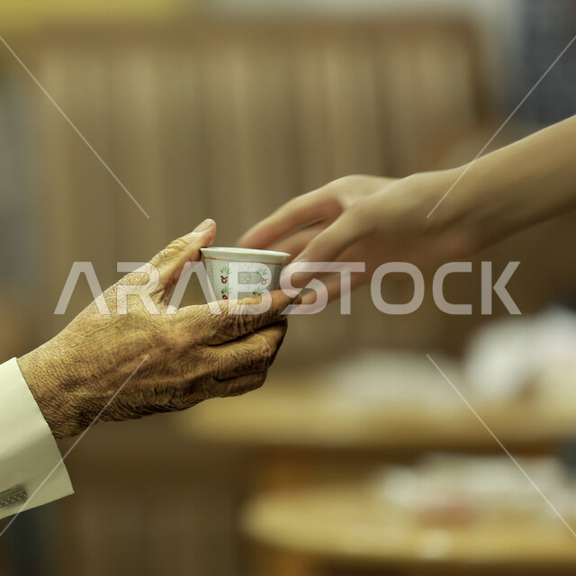 صورة مقربة ليد شخص يقدم كوب من القهوة الصغير، مشروب القهوة الساخن، فنجان قهوه ساده، كافيهات ومطاعم، الصيافة والاستقبال والترحيب، القهوه العربية الخليجية، ضيافة رمضانية