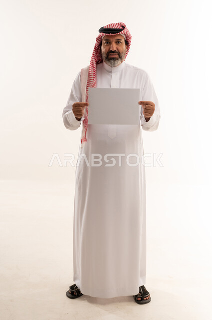 رجل سعودي يحمل ورقة بيضاء فارغة في الاستوديو