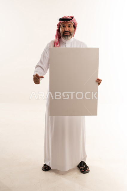 رجل سعودي يحمل لوحة بيضاء فارغة في استوديو