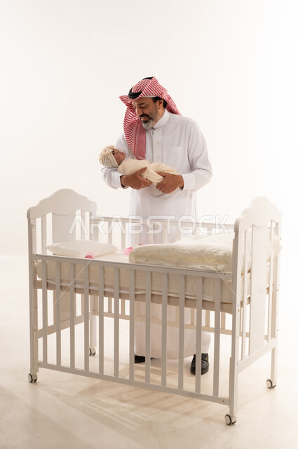 Saudi Grandfather Holding Newborn Baby by White Crib