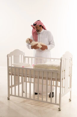 Saudi Grandfather Holding Newborn Baby by White Crib