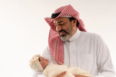 رجل سعودي يحمل طفلاً حديث الولادة نائماً في الاستوديو